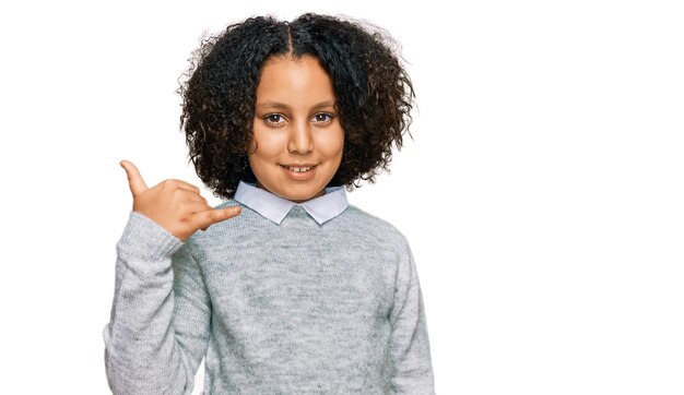 Niña pequeña con cabello afro vistiendo ropa informal sonriendo haciendo gestos telefónicos con la mano y los dedos como hablar por teléfono comunicando conceptos