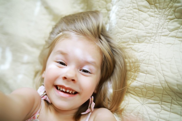 Una niña pequeña con cabello rubio yace en la cama La niña está jugando en el sofá