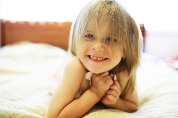 Una niña pequeña con cabello rubio yace en la cama La niña está jugando en el sofá