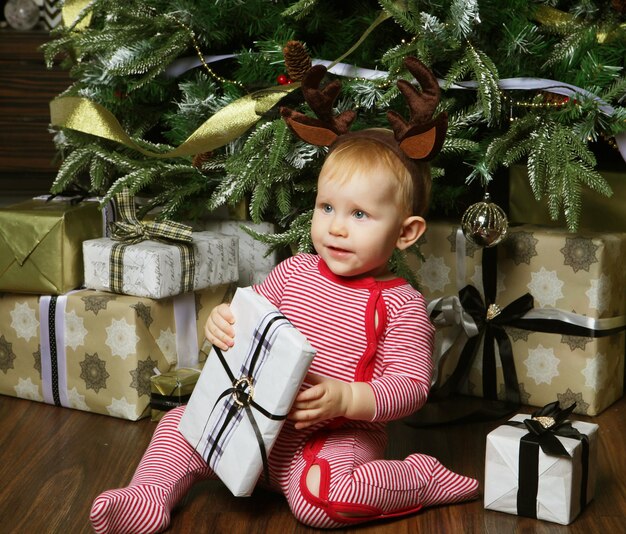 Niña pequeña con la caja de regalo cerca de Decorar el árbol de Navidad Tiempo feliz