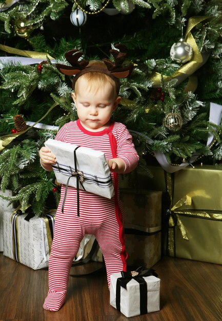 Niña pequeña con la caja de regalo cerca de Decorar el árbol de Navidad Tiempo feliz