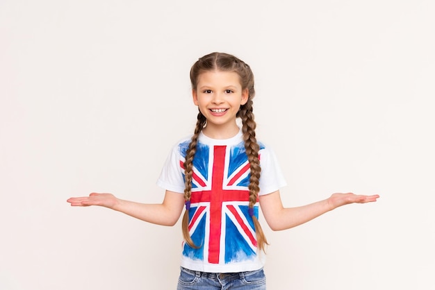 Una niña pequeña con una camiseta con una bandera británica sostiene su anuncio Cursos de inglés para escolares y niños