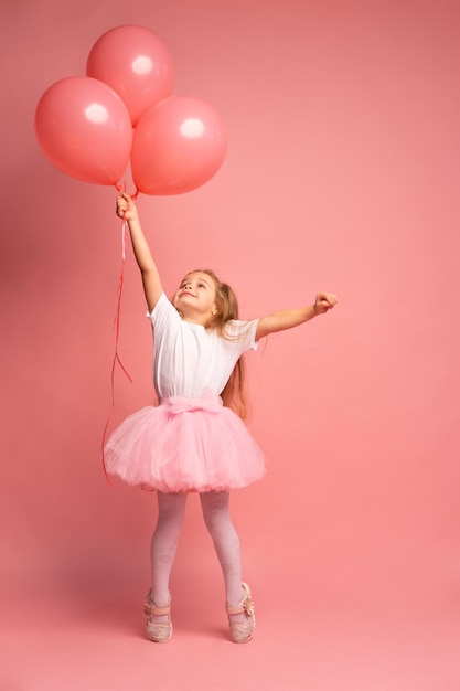 Niña pequeña con una camiseta blanca y un tutú rosa con globos sobre fondo rosa Lista para volar alto