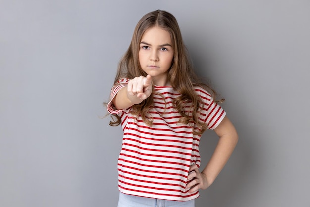 Niña pequeña con camiseta notando y señalando con el dedo a la cámara acusando con una cara mandona seria