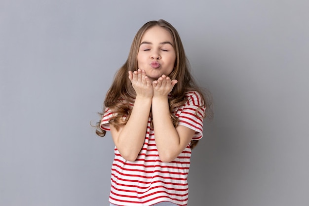 Niña pequeña con camiseta que envía un beso al aire con los labios poutos experimentando los primeros sentimientos románticos