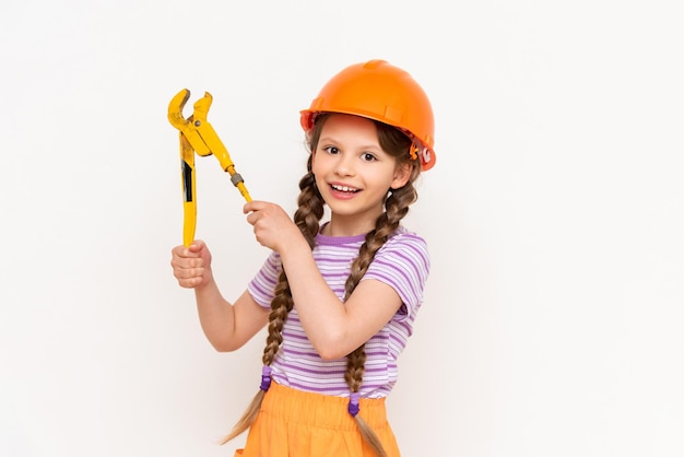 Una niña pequeña con un casco de construcción naranja sostiene una llave inglesa sobre un fondo blanco aislado El concepto de renovación en la habitación de los niños