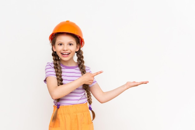 Una niña pequeña en un casco de construcción sostiene su anuncio en su mano sobre un fondo blanco aislado El concepto de renovación en la habitación de los niños