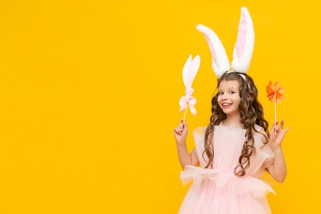 Una niña pequeña celebra la Pascua Un niño sonriente feliz sostiene algunas flores de origami Un adolescente encantador con orejas de conejo sobre un fondo amarillo aislado Copiar espacio Banner