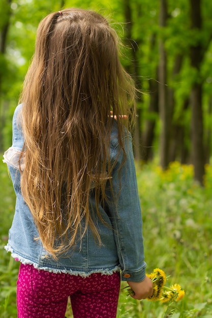 Niña pequeña con una chaqueta vaquera sobre un fondo de pradera primaveral con un ramo de dientes de león en la espalda