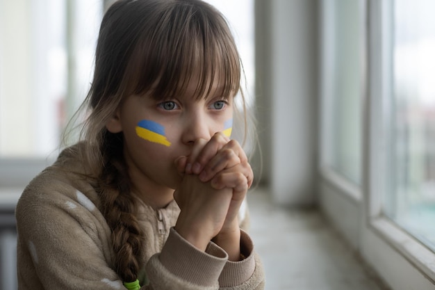 Niña pequeña con cinta de bandera ucraniana rezando Símbolo de paz y rezando por Ucrania