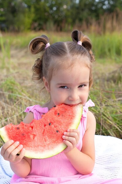 Niña pequeña comiendo rodajas de sandía en el jardín sentada en una hamaca