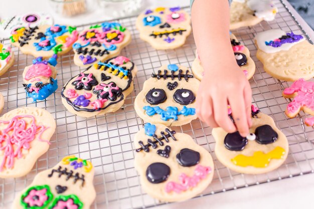 Niña pequeña decorando galletas de azúcar con glaseado real para la festividad del Día de los Muertos.