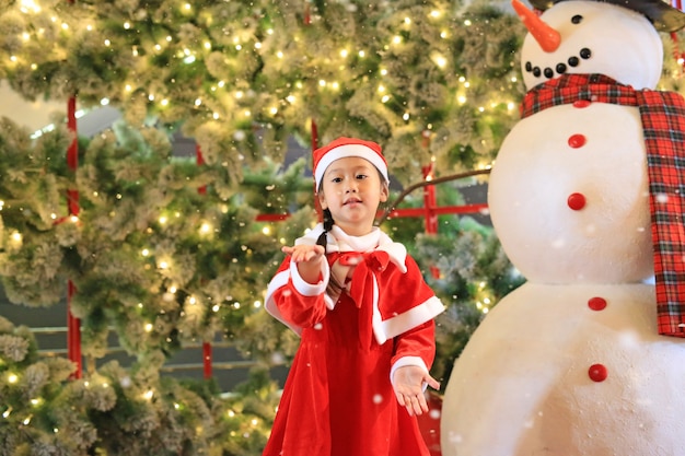 La niña pequeña con disfraz de santa se divierte y juega con la nieve en invierno