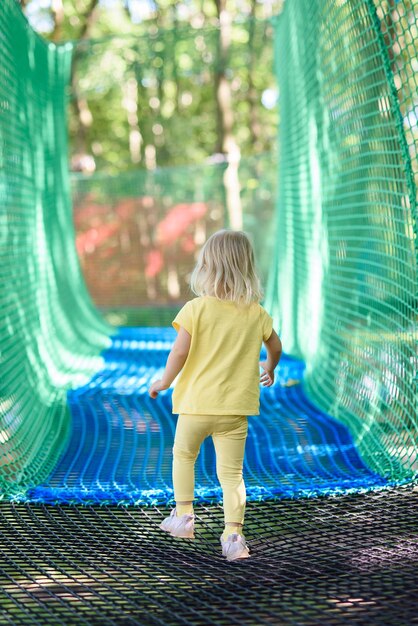 Niña pequeña divirtiéndose en un patio de recreo de cuerdas la niña está jugando en cuerdas de red