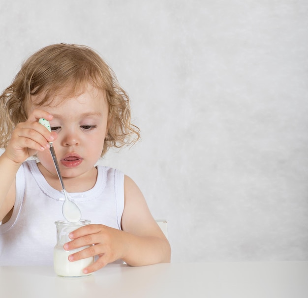 Foto niña pequeña de dos años está comiendo yogur natural sin azúcar. de cerca