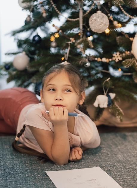 Niña pequeña escribe la carta de Santa Claus y sueña con un regalo de fondo Árbol de año nuevo en el interior. Feliz Navidad y Felices Fiestas.