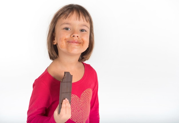 Una niña pequeña está comiendo chocolate con leche contra el fondo blanco aislado