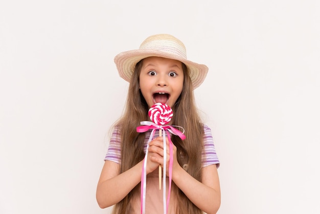 Una niña pequeña está comiendo una piruleta sobre un fondo blanco aislado Un niño come dulces en un sombrero de verano de paja
