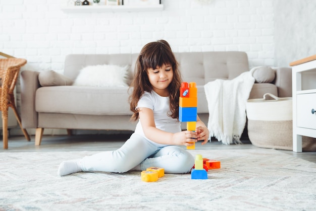 Una niña pequeña está jugando con un constructor de color en casa en el suelo.