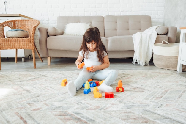 Una niña pequeña está jugando con un constructor de color en casa en el suelo.