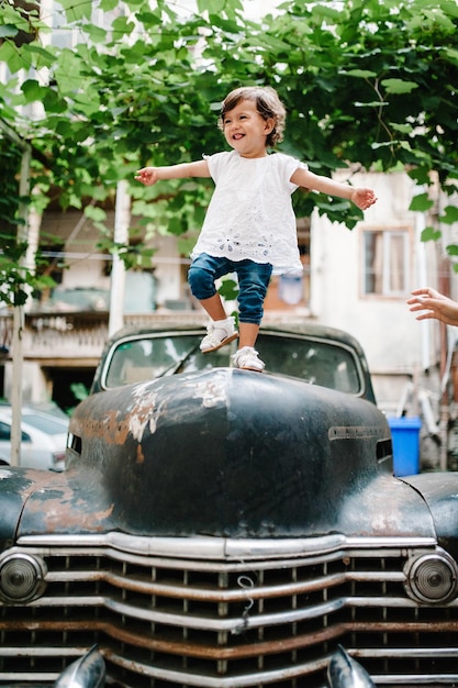 La niña pequeña está de pie en un antiguo auto antiguo Familia feliz joven durante un paseo por la calle del casco antiguo al aire libre El concepto de vacaciones familiares y viajes La madre sostiene a la niña