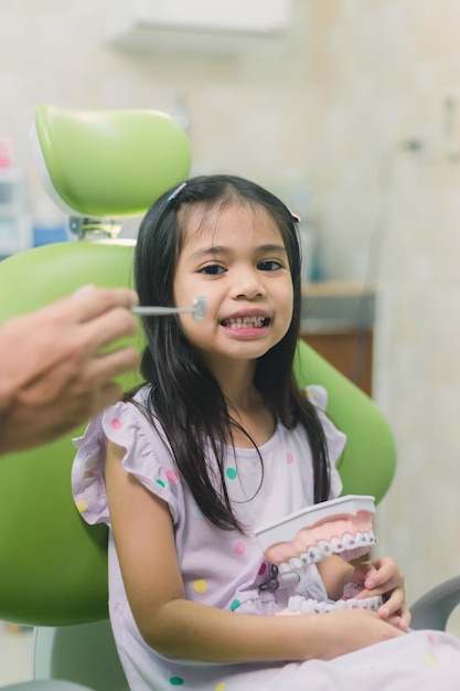 Una niña pequeña está sentada en una silla de dentista y le están cepillando los dientes.