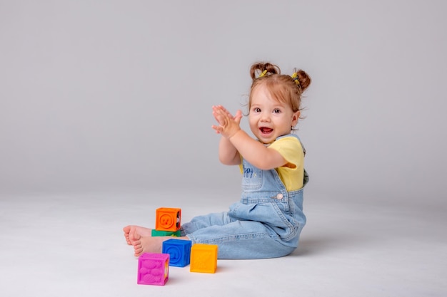 la niña pequeña está sentada sobre un fondo blanco y jugando con cubos coloridos. juguete para niños