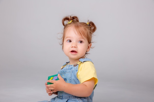 la niña pequeña está sentada sobre un fondo blanco y jugando con cubos coloridos. juguete para niños