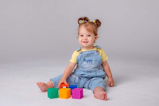 la niña pequeña está sentada sobre un fondo blanco y jugando con cubos coloridos. juguete para niños