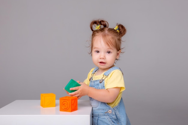 la niña pequeña está sobre un fondo blanco y juega con cubos coloridos cubos de juguete para niños