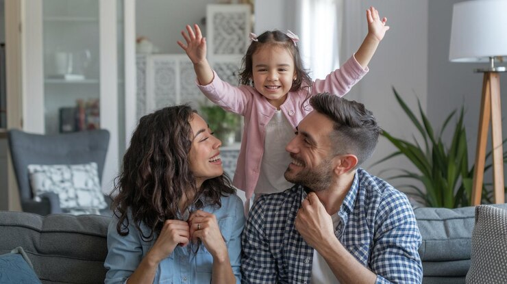 una niña pequeña está sonriendo y sus padres están animando a la cámara