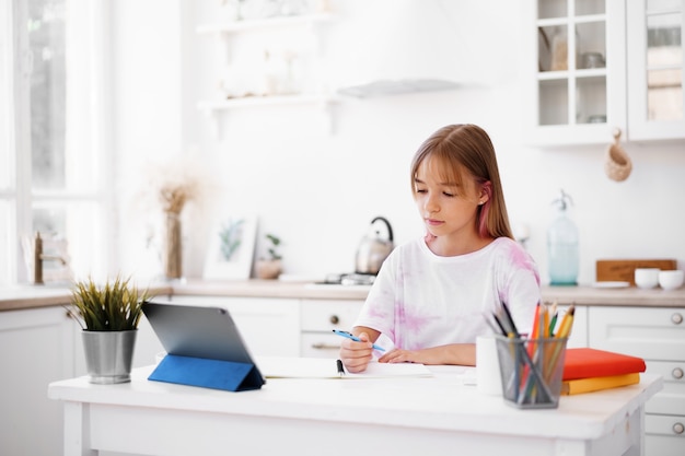 Niña pequeña estudiante educada en el hogar que tiene clase en línea con tableta digital