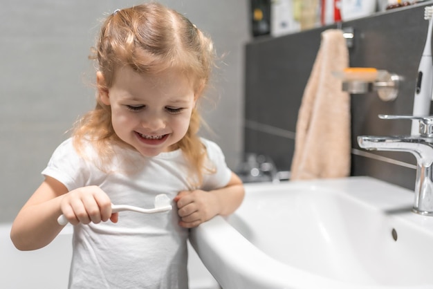 Niña pequeña feliz cepillando los dientes en el baño