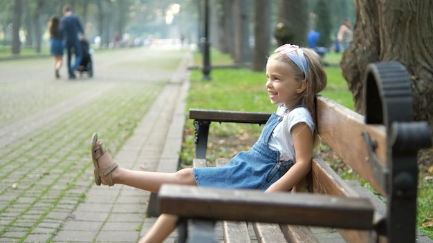 Niña pequeña feliz sentada en un banco sonriendo alegremente en el parque de verano