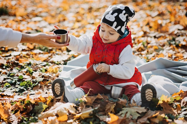 Niña pequeña feliz con termo rojo y taza en picnic de otoño en la naturaleza de otoño