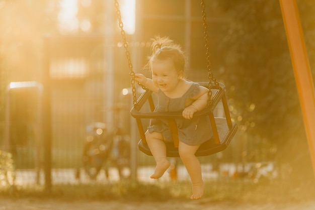 Una niña pequeña feliz con un vestido en un columpio en la cálida noche de verano