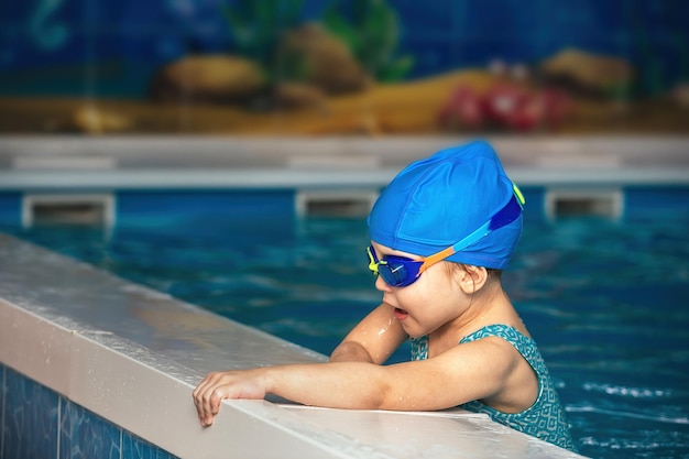niña pequeña con gafas impermeables y traje de baño en una clase de natación en una piscina cubierta