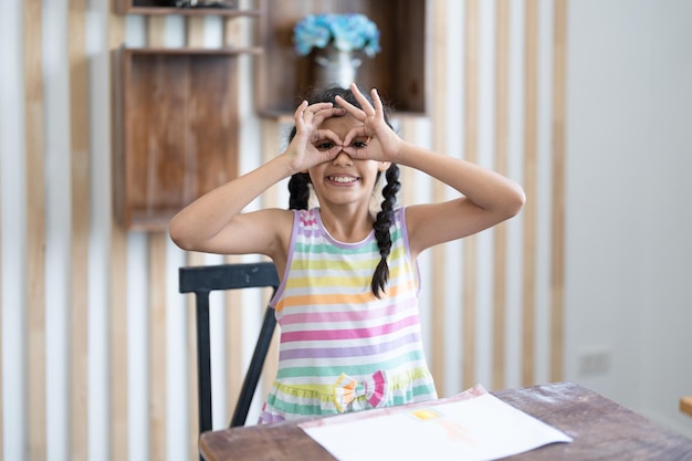 Niña pequeña con gafas de manos delante de los ojos y sentada en el aula de la escuela primaria