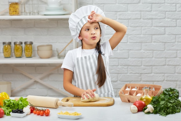 Niña pequeña con gorra y delantal amasa la masa