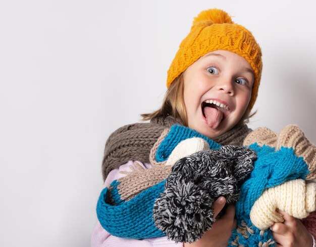 Niña pequeña con gorro de punto bufanda y suéter sosteniendo un montón de sombreros