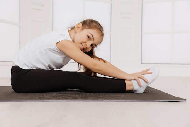 Niña pequeña haciendo ejercicios de estiramiento y gimnasia en casa con un fondo blanco