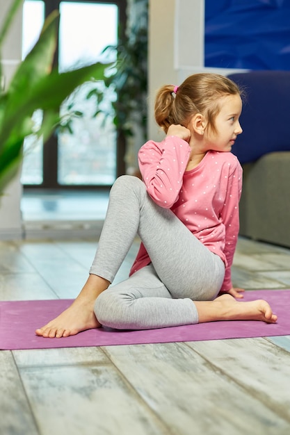 Niña pequeña haciendo ejercicios de estiramiento, practicando yoga en la alfombra de fitness en casa