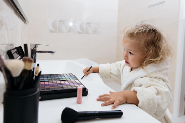 Niña pequeña haciendo maquillaje con sombras de ojos en bata de baño