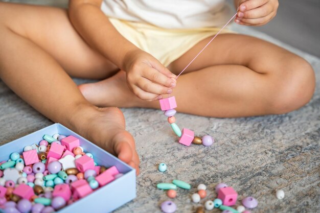 Foto niña pequeña haciendo pulseras de cuentas de madera en casa sala de estar creatividad infantil y el