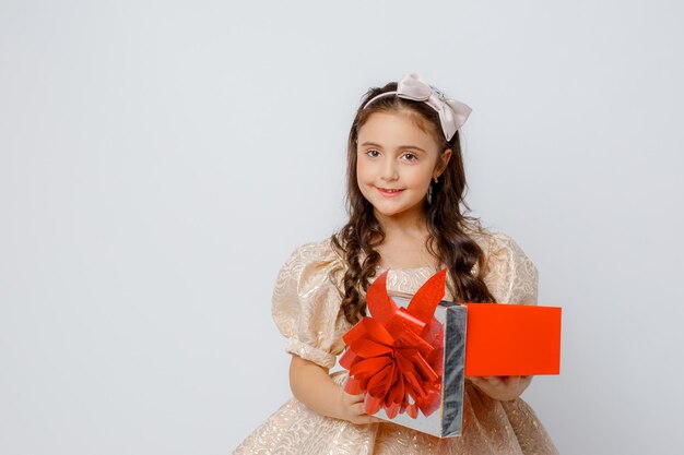 Una niña pequeña con un hermoso vestido sostiene una caja de regalo en un fondo blanco