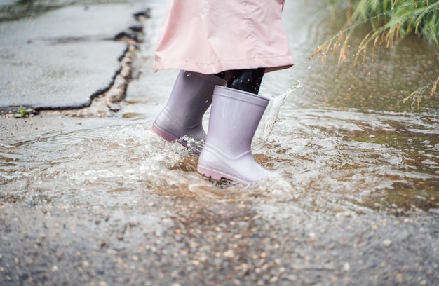 Niña pequeña con impermeable rosa impermeable botas de goma moradas salta divertida a través de charcos en la calle en días lluviosos Primavera otoño Diversión infantil después de la lluvia Actividad recreativa al aire libre