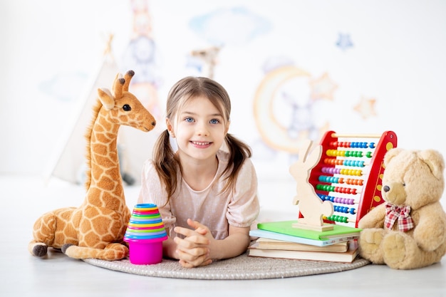 una niña pequeña juega con juguetes en una alfombra en una habitación infantil brillante construyendo una pirámide tendida en el suelo un niño sonriente en casa jugando al desarrollo preescolar temprano