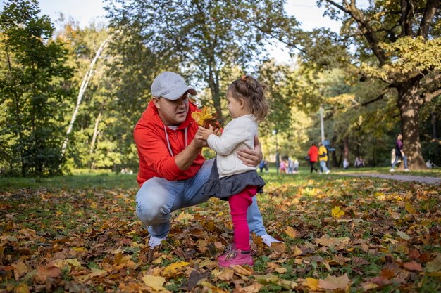 Niña pequeña juega con el padre al aire libre en el parque de otoño