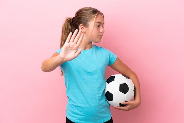 Niña pequeña jugadora de fútbol aislada de fondo rosa haciendo un gesto de parada y decepcionada