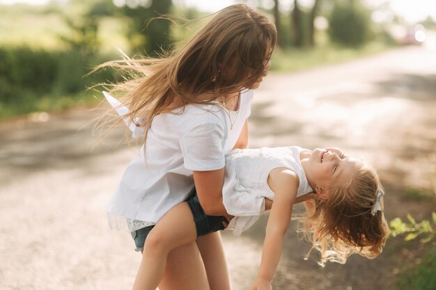 Niña pequeña jugando con mamá en el parque en el día de verano durante la puesta de sol